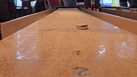 people playing shuffleboard viewed from close to table at end people playing shuffleboard viewed from close to table at end