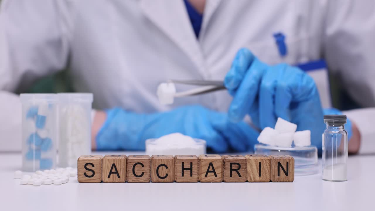 Blocchi di parole 'Saccarina' con scienziato che manipola dolcificante artificiale in laboratorio