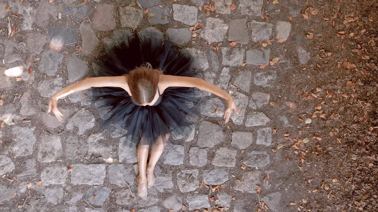 검은 투를 입은 젊은 발레 댄서가 야외에 앉아 팔을 움직인다