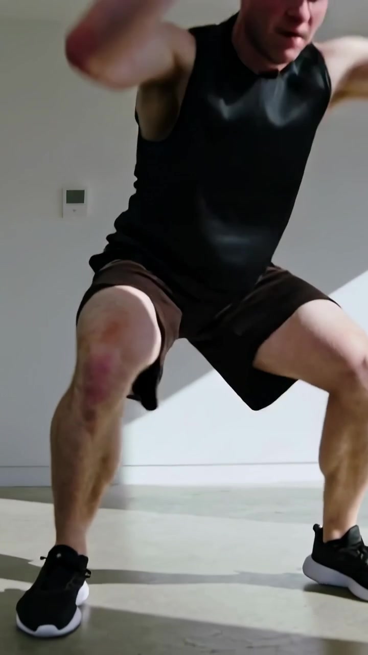 Video verticale: Uomo atletico con maglietta nera che inizia a fare burpees in una stanza vicino al termostato per il fitness.
