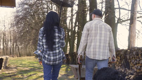 vista trasera de una pareja caucásica y su perro caminando por el campo. el hombre lleva una carretilla