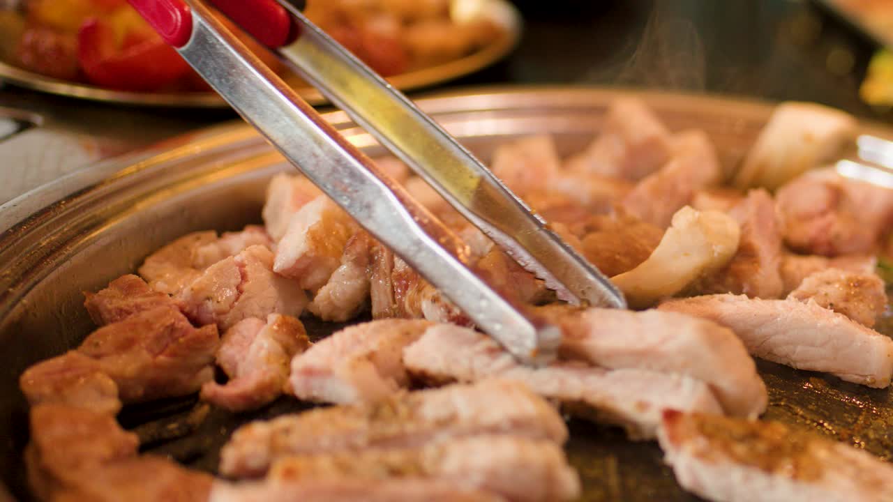 Close-up of pork belly being cut and grilled on a hot Korean barbecue grill pan