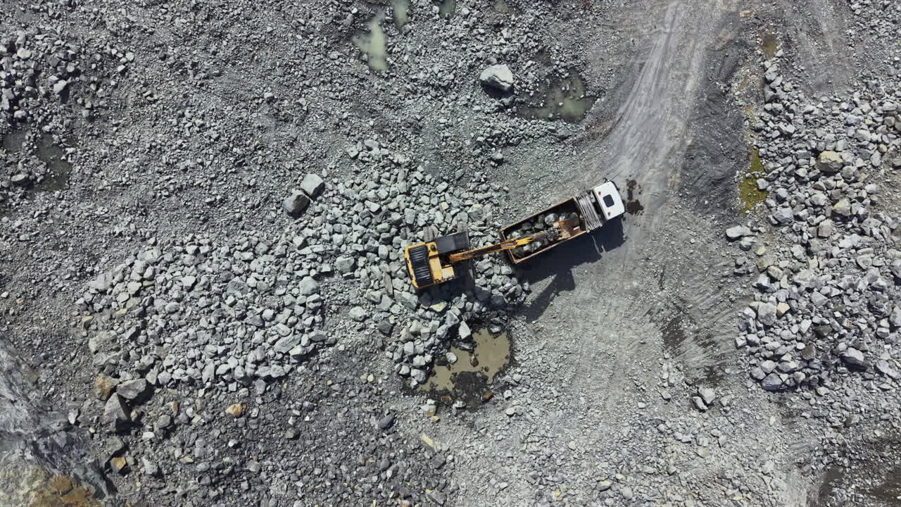 Activity at granite quarry shows truck and excavator transporting rocks and minerals