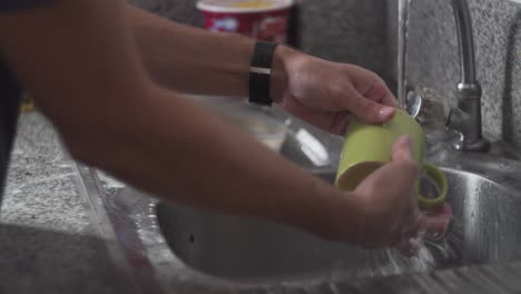 manos de la persona con agua corriente del grifo, enjuague y limpieza de platos sucios