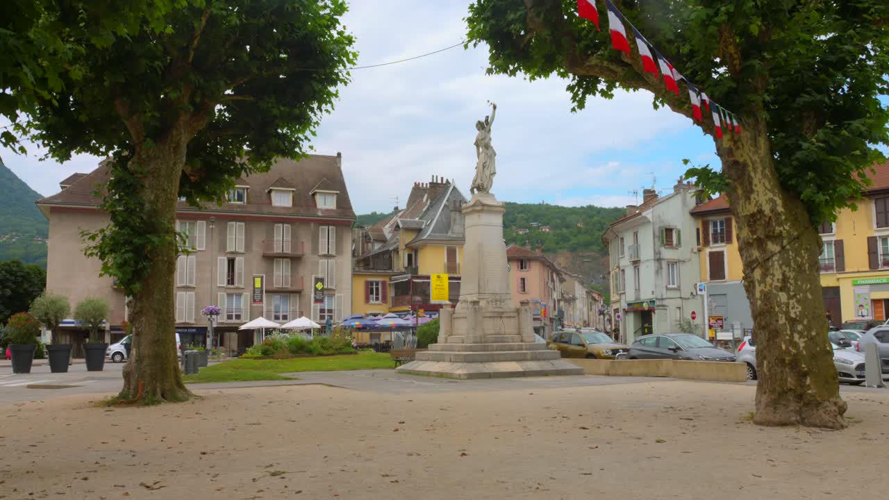Statue in the town center of Vizille France surrounded by trees buildings and festive flags