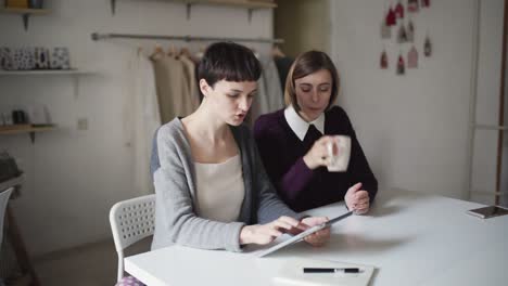 two creative woman using tablet for new project on background hanging clothes