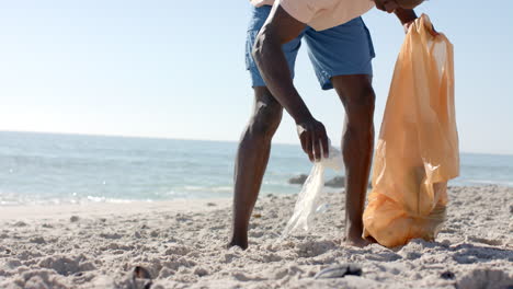 a young african american man collects trash on the beach