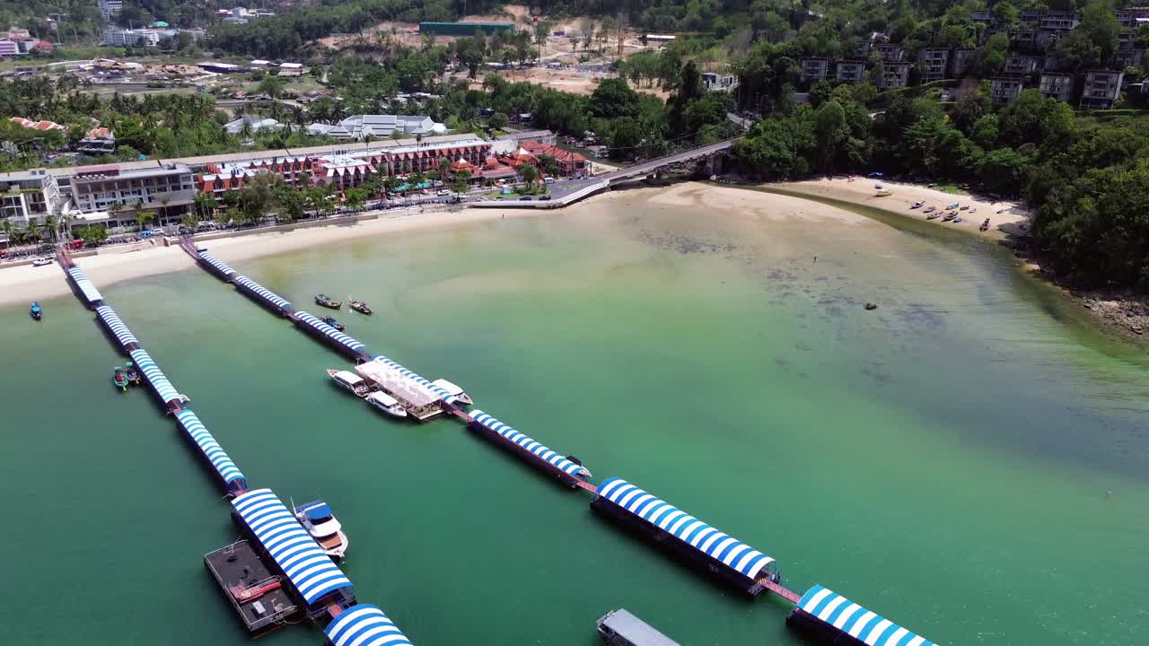 Drone films a harbour with piers in Patong, Phuket. A boat moves between the piers as the camera pans up to reveal the stunning skyline and coastal cityscape of Thailand.