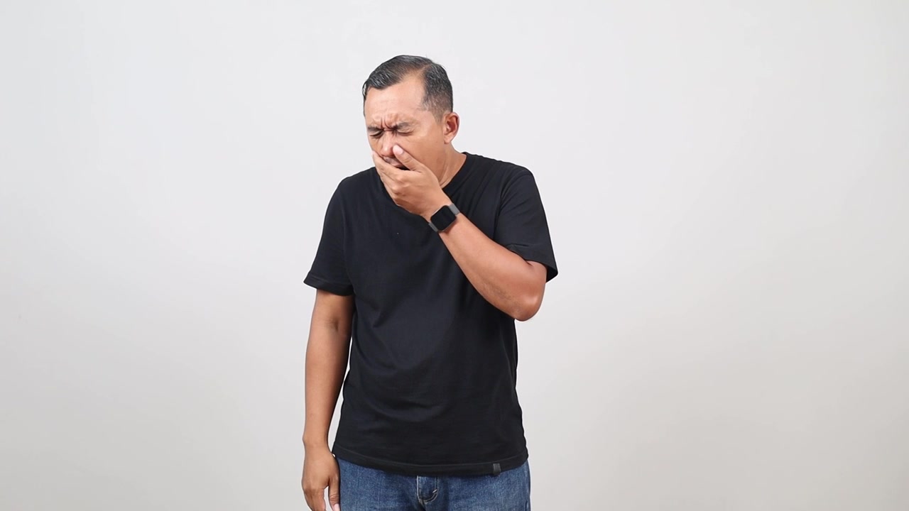 Uomo asiatico in abiti casual, stanco o annoiato, che sbadiglia e si copre la bocca, isolato su sfondo bianco