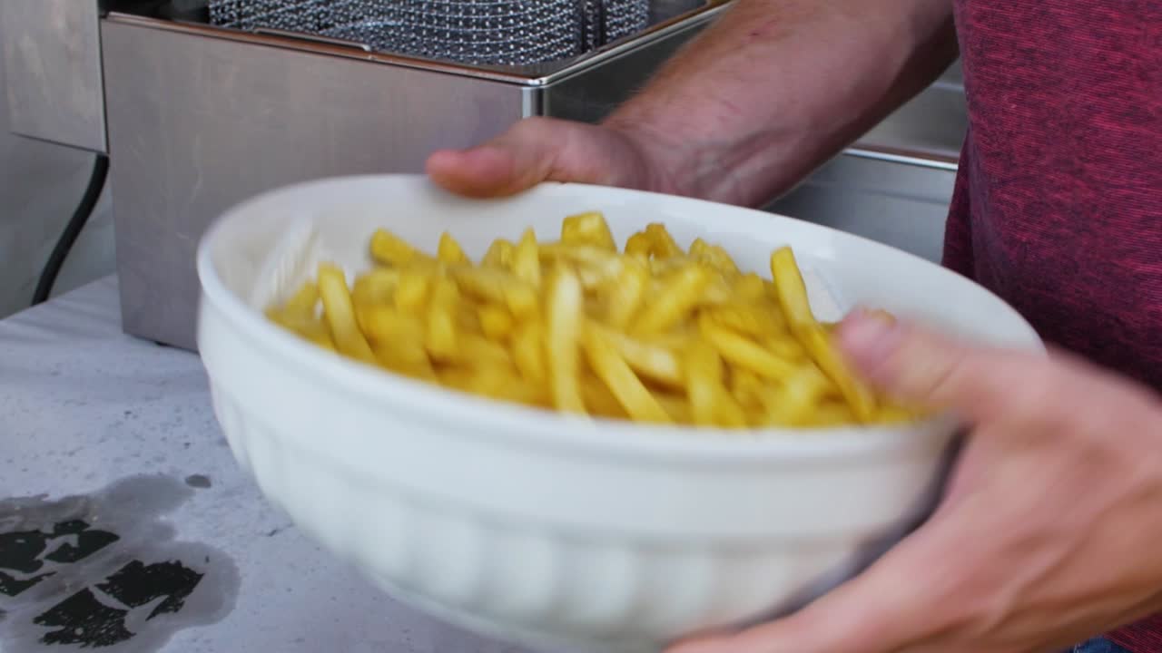 Crispy french fries being shuffled in white bowl to spread the salt