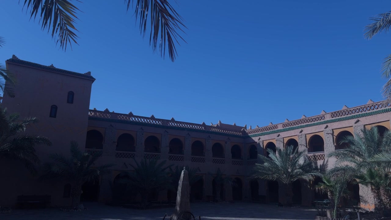 Cortile di una kasbah marocchina caratterizzato da arcate ad arco, muri di argilla e palme sotto un cielo blu