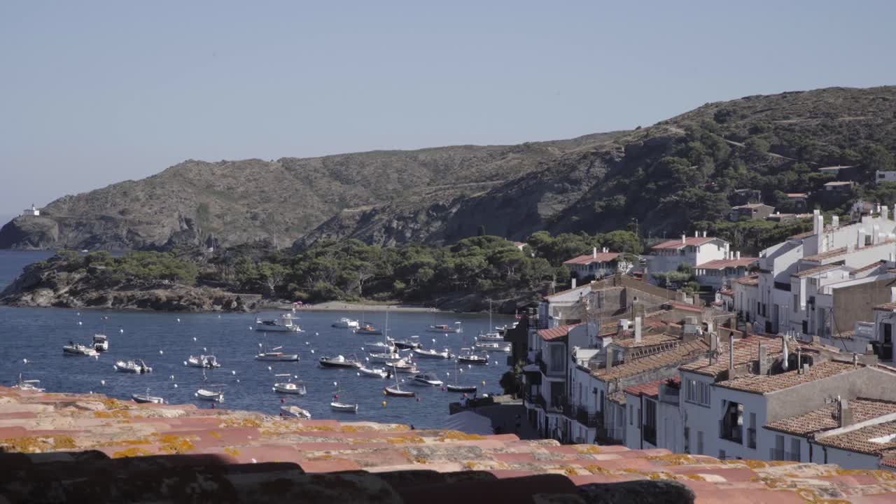 Coast town in Costa Brava, Spain, boats in the ocean, roof in the foreground, mountains, clear sky, static shot