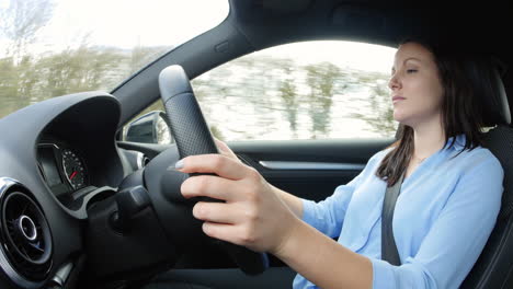 young woman driving in a car in a rural setting, waist up