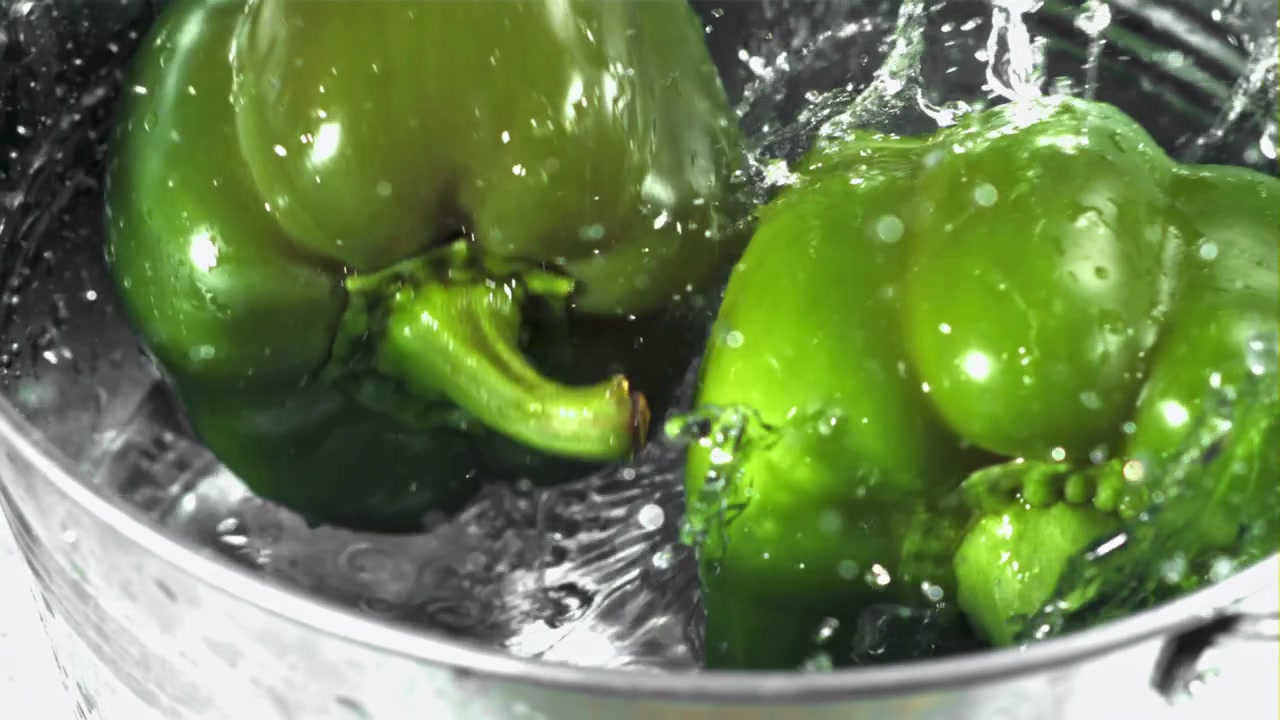 スローモーションで水しぶきを上げて水に落ちる新鮮な緑のピーマン