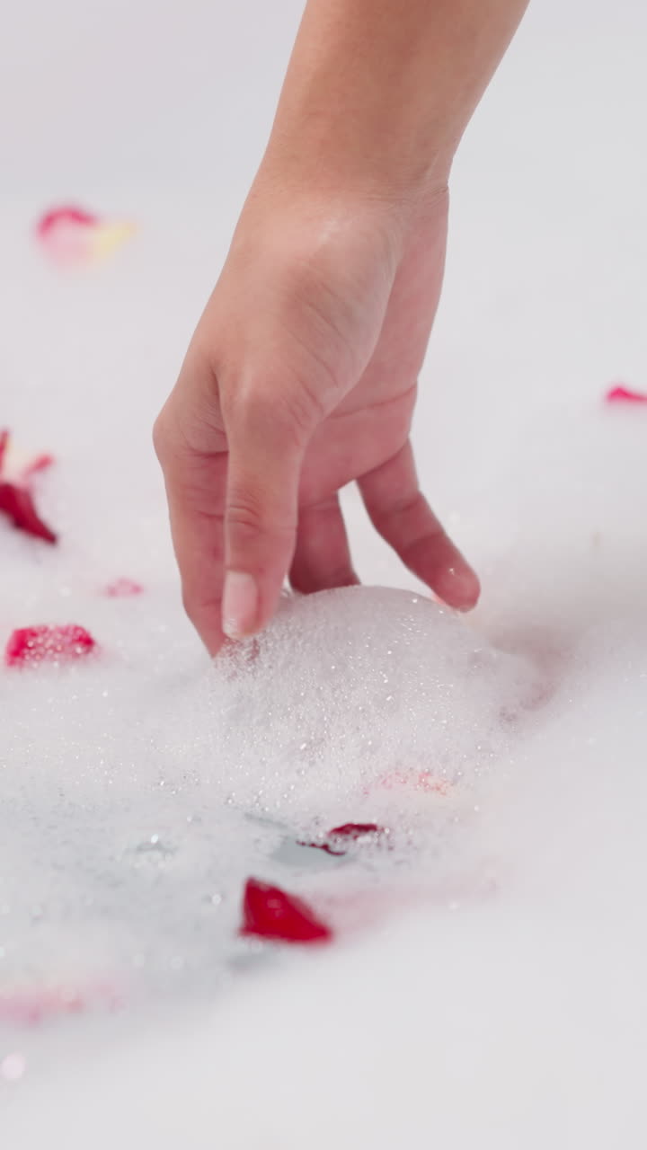 여성은 장미 잎자루를 가까이에서 어내는 거품을 니다. 여자는 호텔 방 욕조에서 자연 꽃으로 향기있는 거품 목욕을 즐니다. 신체 관리의 고급스러운 의식