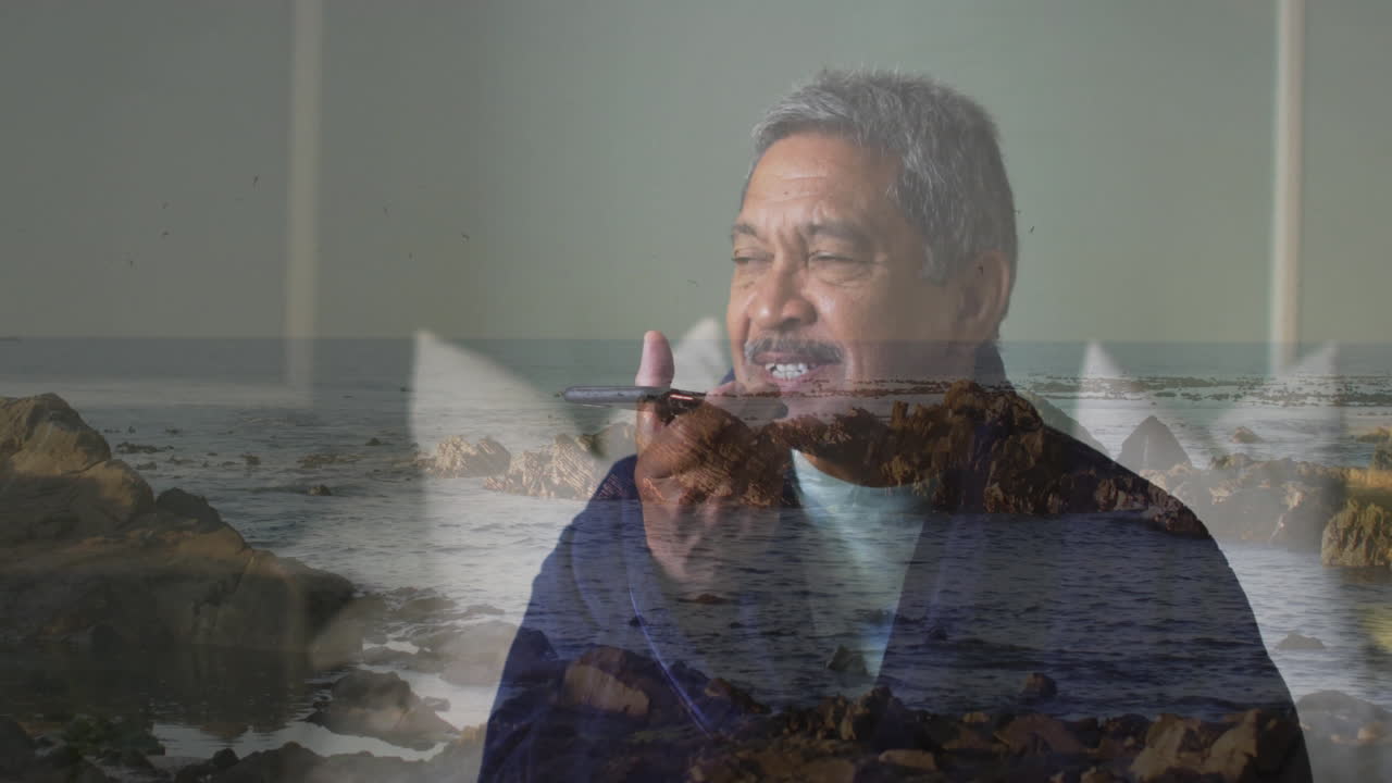 Talking on phone, elderly man standing on rocky ocean shoreline
