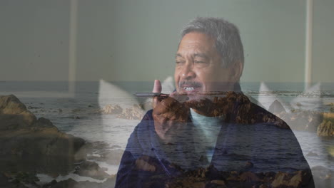 talking on phone, elderly man standing on rocky ocean shoreline