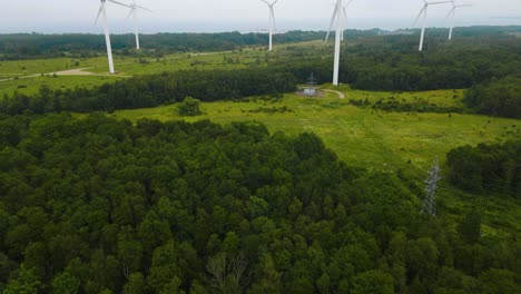 aerial drone revealing footage shot of large white renewable energy electrical power creating wind turbines on a green forest covered peninsula during a cloudy day. footage flying backwards smoothly