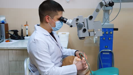 young male student of medical university practices on dummy. future dentist uses drill and looks at microscope. side view.