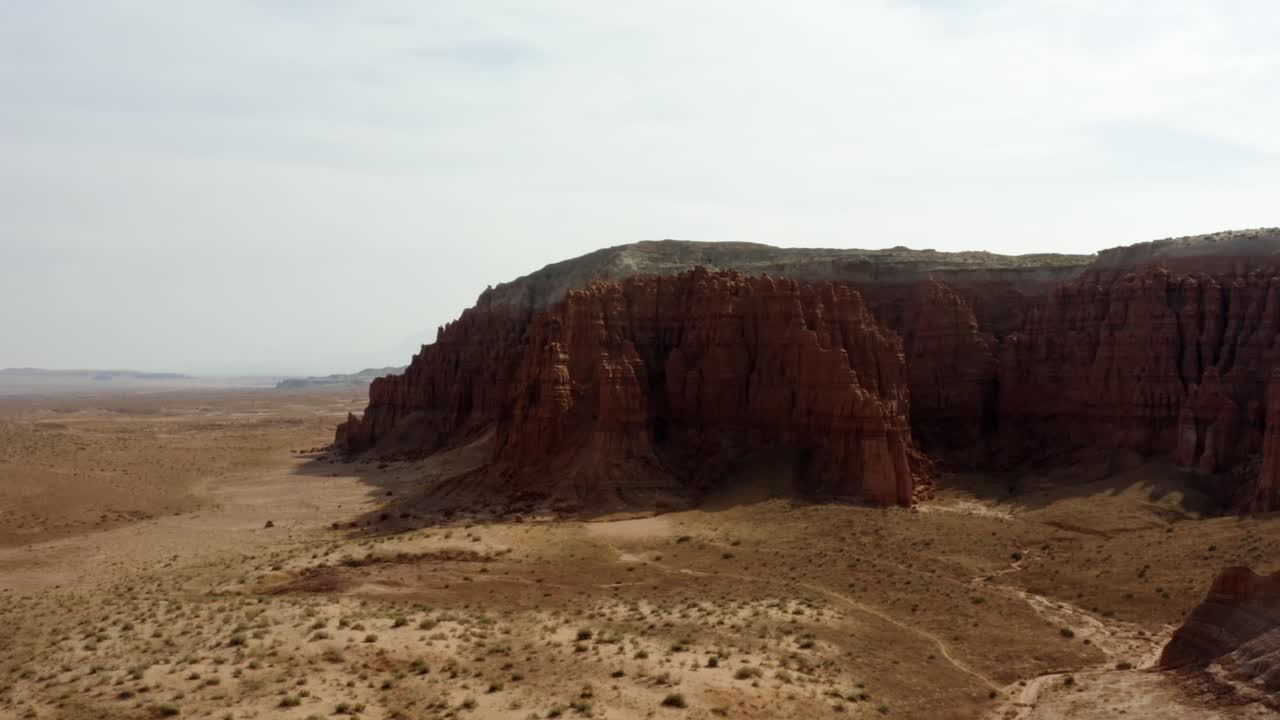 Gorgeous rising aerial drone shot of the beautiful Goblin Valley Utah State Park with a valley of red sand and large red and white Butte's in the background