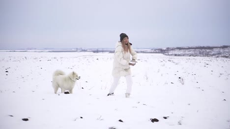 young woman outdoor enjoying first snow with family and dog, throwing a snowball