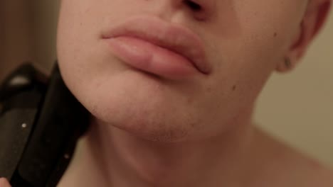 close up shot of a young person using an electric trimmer on the side of their face and chin