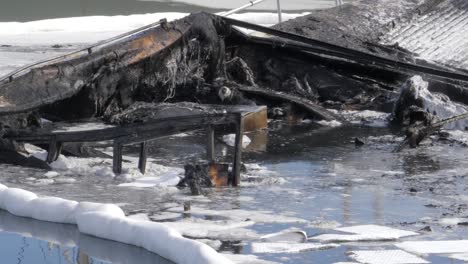 a burnt boat floats in the water with a protective oil boom around it to help prevent further water pollution