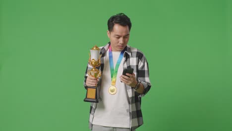 hombre sosteniendo el trofeo y la medalla, mirando el teléfono inteligente