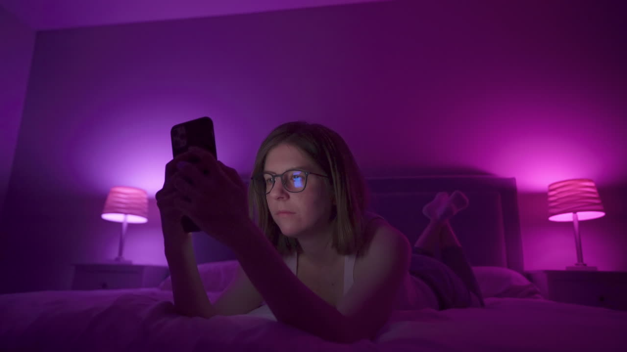 Girl browses social media on smart phone late at night in bedroom.
