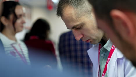 mid-aged caucasian man wearing white robe looks down talking. neurosurgery trainer works in a group of learners.
