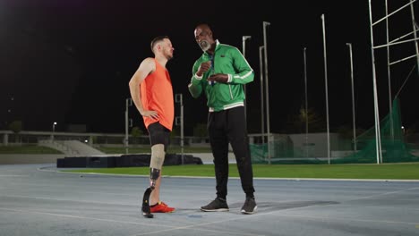 entrenador masculino diverso y atleta masculino discapacitado con hoja de correr de pie y hablando