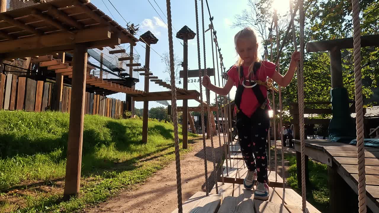 niña feliz jugando en la atracción de tarzán en el patio de recreo en el parque de atracciones