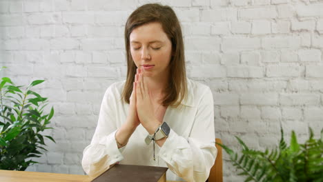 una mujer joven orando con una biblia y las manos juntas en oración