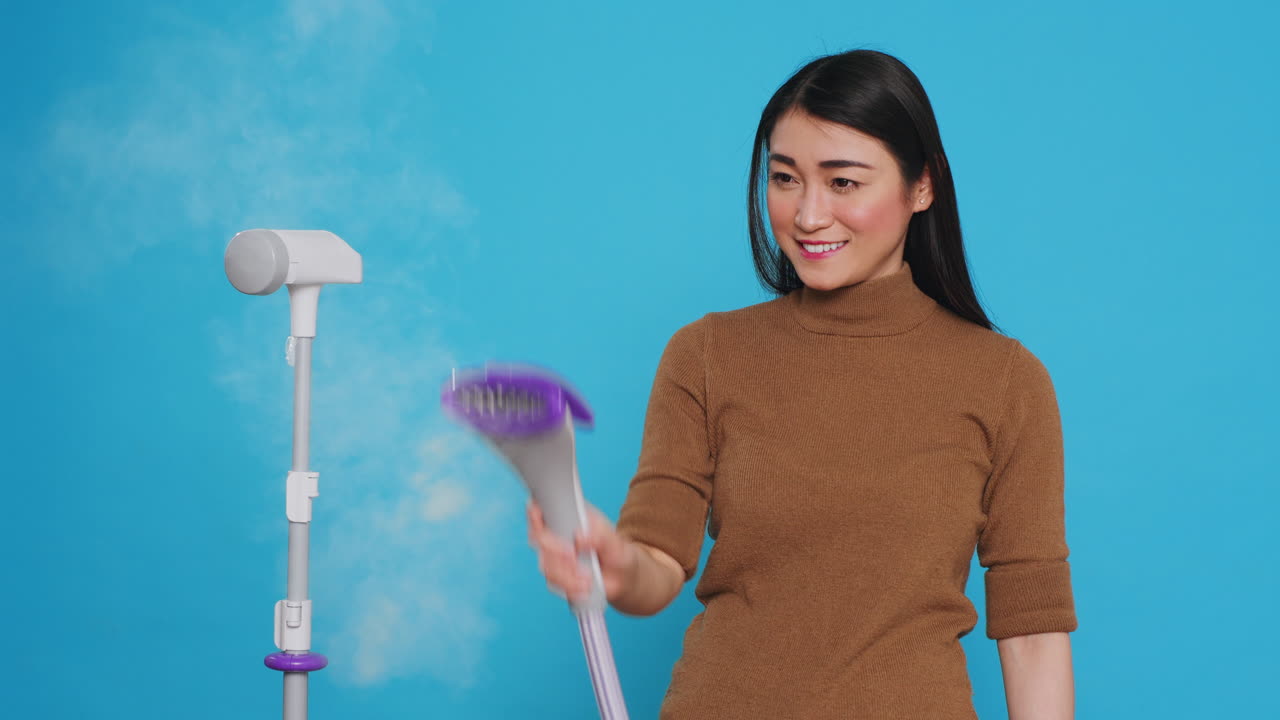 Smiling cleaning lady using steamer to ironing clothes in studio