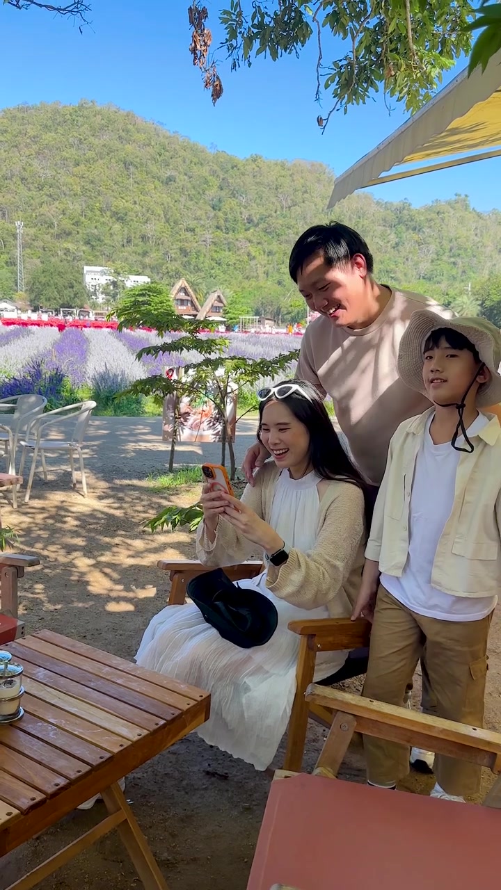 แม่ พ่อ และลูกชายกำลังดูสมาร์ทโฟนด้วยกันกลางแจ้งท่ามกลางแสงแดดจ้า