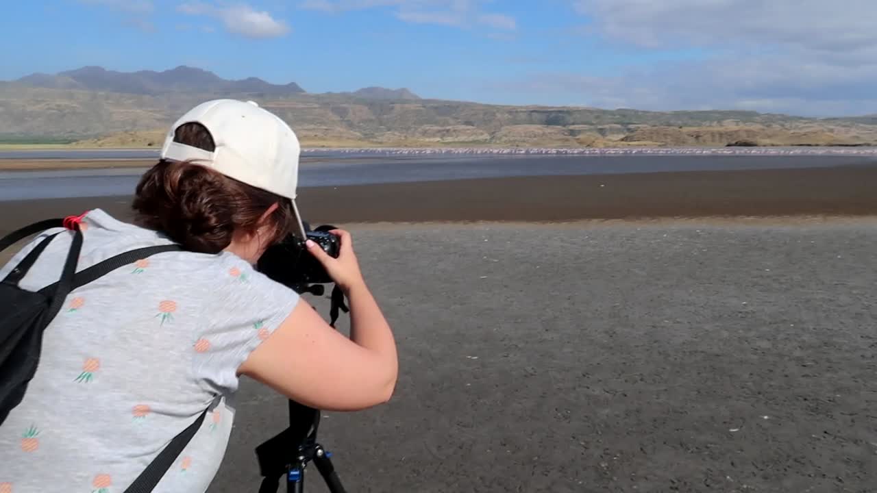 Professional photographer woman taking photos of flamingos at a lake in Africa