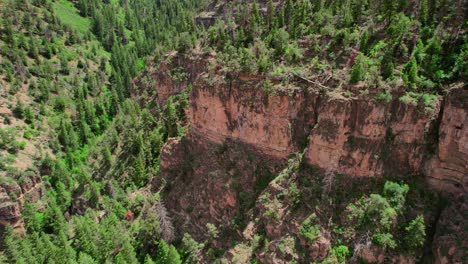 Tiro-De-Drone-Hd-Volando-Sobre-El-Acantilado-Del-Cañón-Rocoso-Cubierto-De-árboles-Verdes-Saludables-Durante-El-Brillante-Día-De-Verano