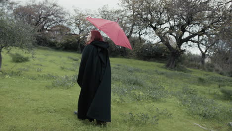 woman walks with red umbrella in a meadow in the countryside in nature