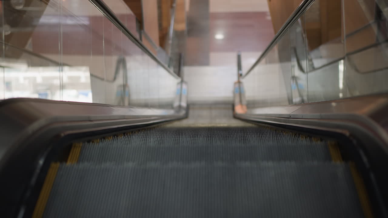 high angle view of automatic moving walkway ascending through glass balustrade in modern shopping mall, empty metallic steps conveying upward motion and sleek architectural lines
