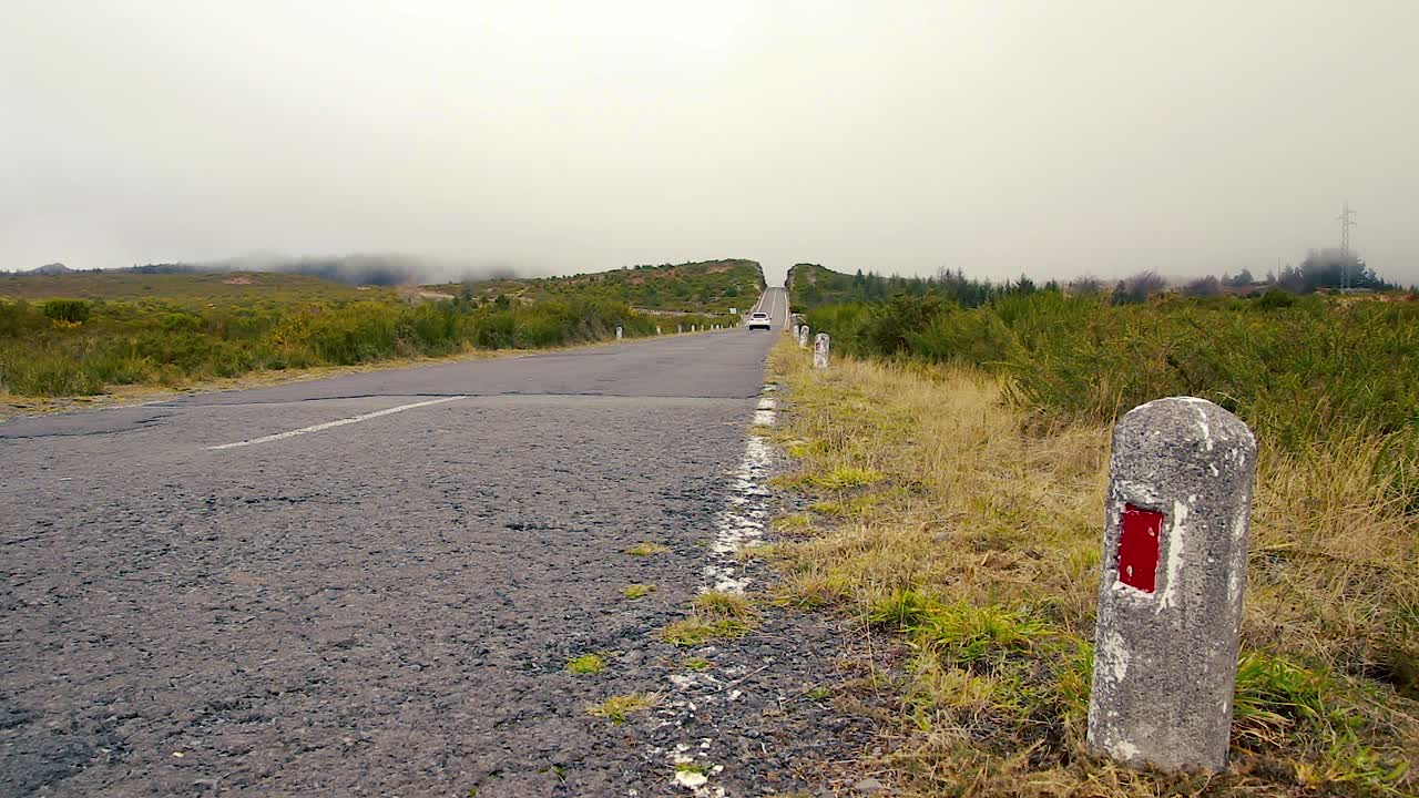 Ground level low angle pov of white car passing on solitary country road