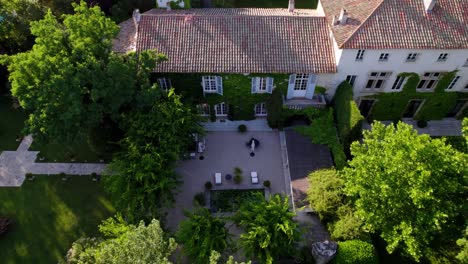 Drohnenaufnahme-Der-Himmelsansicht-Eines-Großen-Hauses-Im-Süden-Frankreichs-Mit-Efeu-An-Einigen-Fassaden,-Einem-Großen-Gebäude-Und-Einem-Großen-Waldgebiet-Drumherum