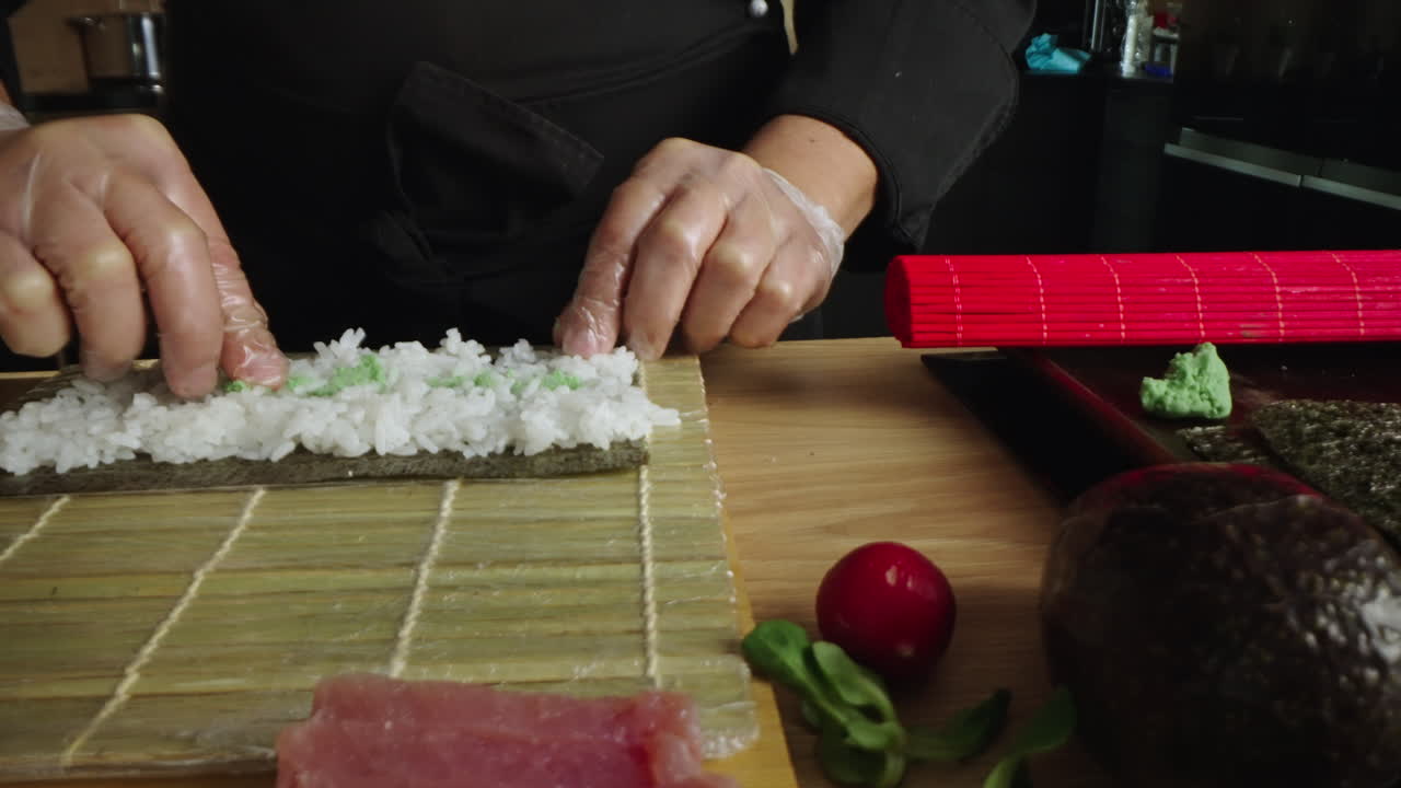 Hands preparing sushi with rice and wasabi on a rolling mat