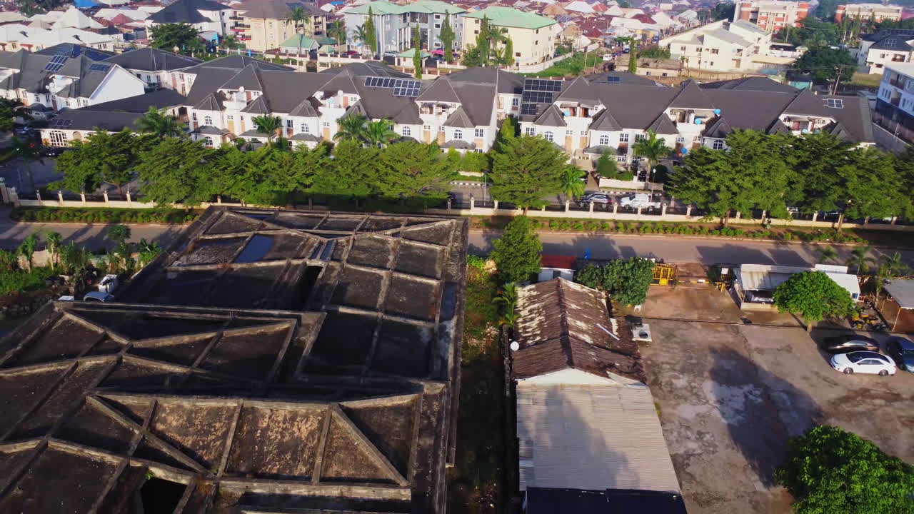 Drone flying away from luxury homes in a beautiful suburban neighborhood in the city of Abuja, Nigeria. Aerial captures concrete rusty rooftop in Gudu neighborhood