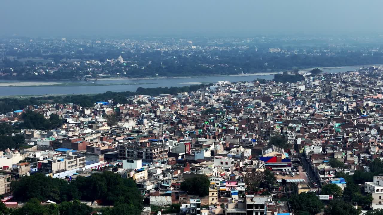 Panorama aereo della città di Mathura che si estende fino alle rive del fiume Yamuna—densi quartieri storici, guglie di templi e punti di riferimento sacri che si fondono con la vita urbana sotto una leggera foschia dell'India settentrionale.