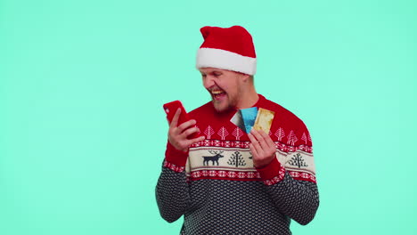 Man-in-Christmas-red-sweater-use-mobile-cell-phone,-plastic-credit-bank-cards,-win,-calebrate,-wow