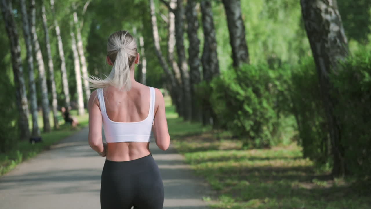 vista trasera de una linda chica rubia corriendo en el parque