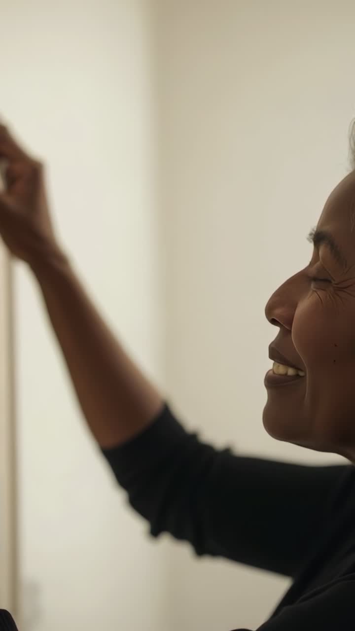 Vertical video: Reaching senior woman in dark top adjusting frame to level on pale wall, copy space