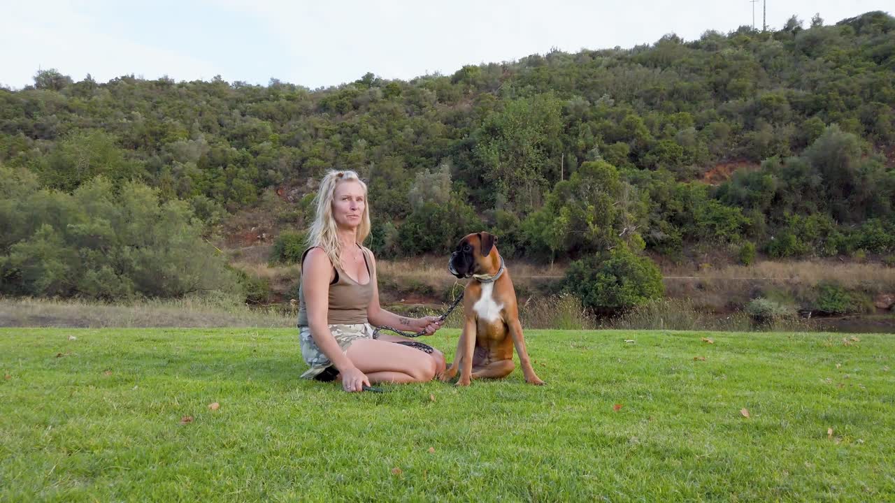 박서 개 가 수술 후 회복 하기 위해 주인 과 함께 공원 의 잔디 에 앉아 있다