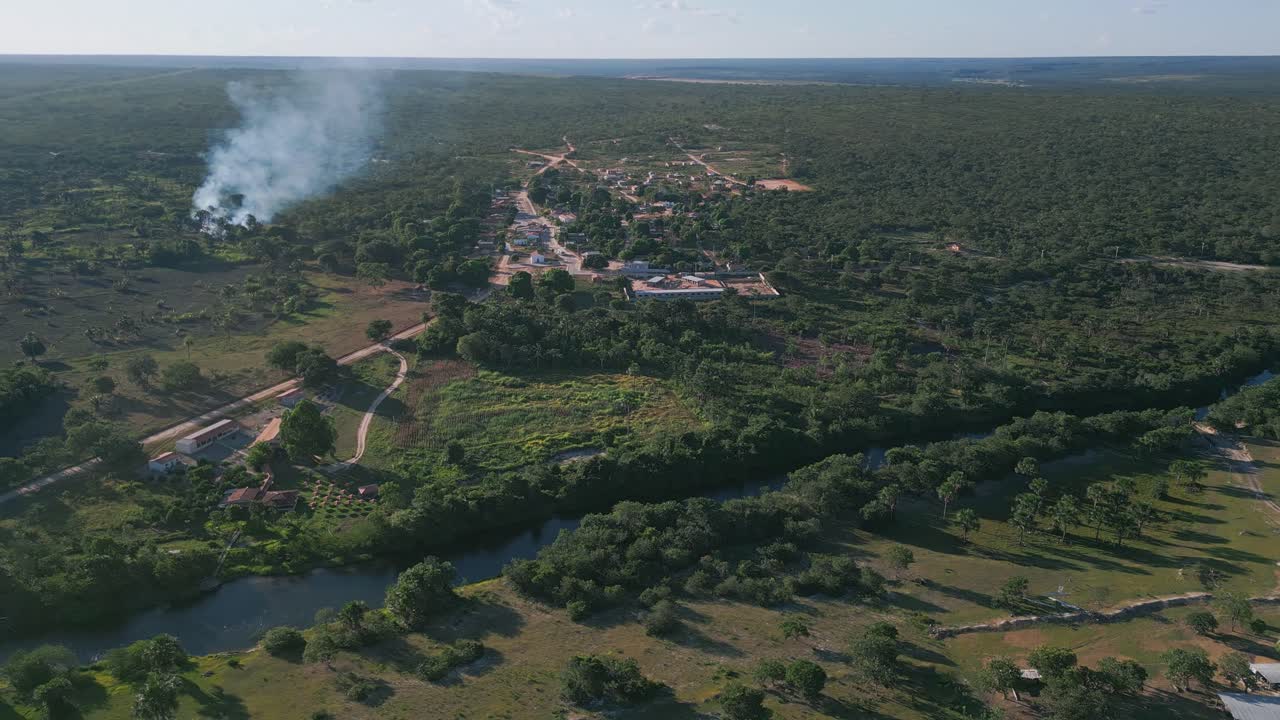 La vista a distanza cattura i drammatici meandri del fiume: un unico sistema perenne e sinuoso di colore blu con margini di foresta a galleria ripariale, insediamento adiacente, attività di gestione degli incendi visibile attraverso l'altopiano