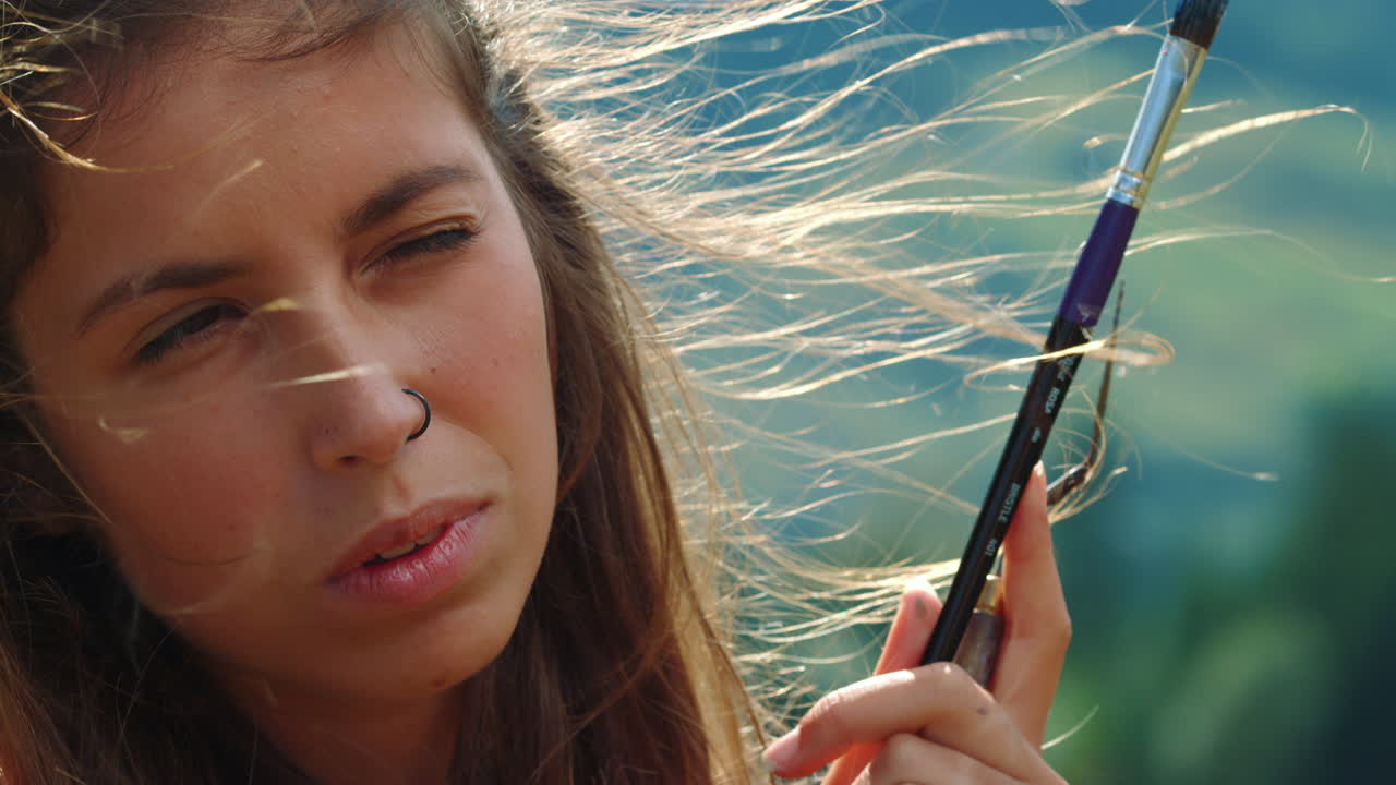 여름 자연에서 일하는 클로즈업 화가. 사려 깊은 소녀는 야외에서 눈을  ⁇ 푸리고 있습니다.